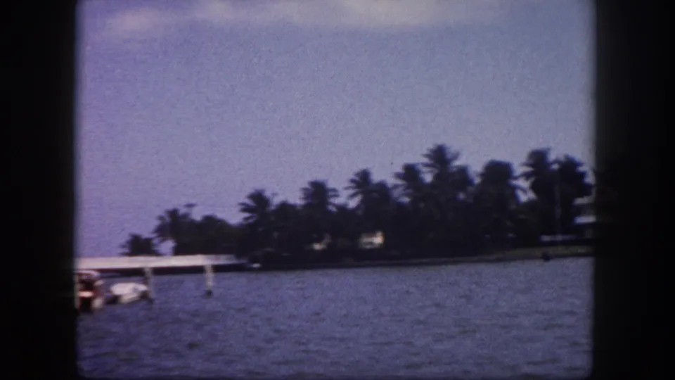 Broad waterway with palm-lined shore, flat dock structure, and small boat; Tampa, Florida, circa 1960, 8mm home movie.