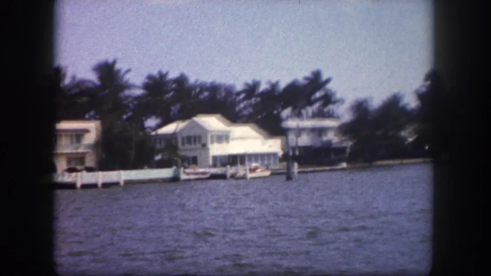 8mm pan shot of white Florida waterfront homes, private dock fencing, and moored boats at the shoreline, Tampa, Florida, circa 1960.