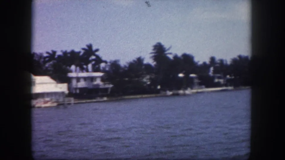8mm footage of white mid-century waterfront estates with moored boats and dense palm trees, Tampa, Florida, circa 1960.