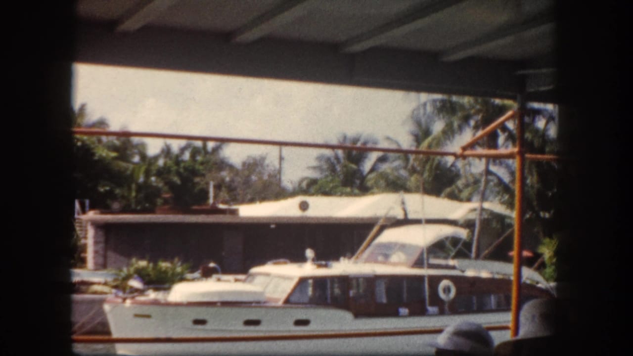 Classic white motor yacht docked at a private waterfront marina, Tampa, Florida area, circa 1960, captured on 8mm home movie film.