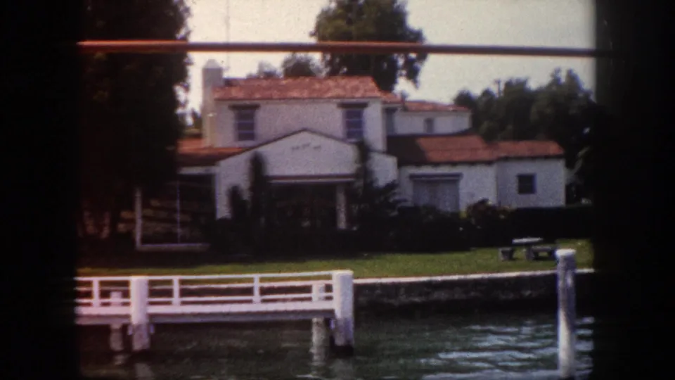 Mediterranean-revival white stucco home with red tile roof on a Tampa, Florida waterfront, circa 1960, viewed from the water with a private dock in the foreground.