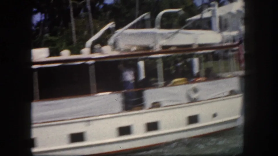 Close view of the hull of a classic circa-1960 white motor yacht, possibly Tampa Bay area, showing porthole details and waterline, shot on 8mm home movie film.