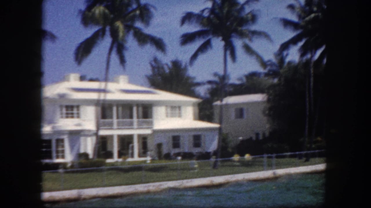 8mm color shot of a white two-story waterfront house with upper balcony and coconut palms, likely Tampa, Florida, circa 1960.