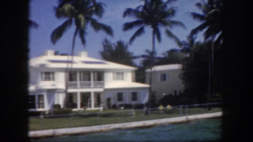 8mm color shot of a white two-story waterfront house with upper balcony and coconut palms, likely Tampa, Florida, circa 1960.