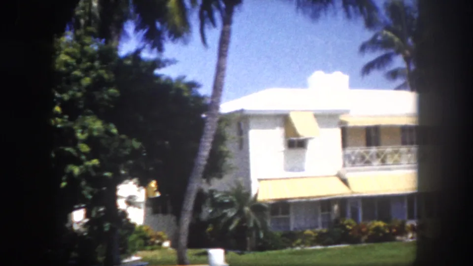 Two-story mid-century Florida house with yellow awnings and tropical garden, no people visible, circa 1960, 8mm color film.