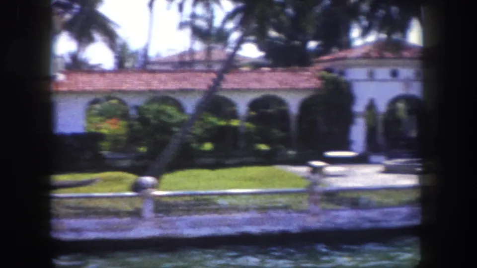 Low Mediterranean Revival building with open arched colonnade and terracotta tile roof filmed from a Tampa canal, circa 1960.