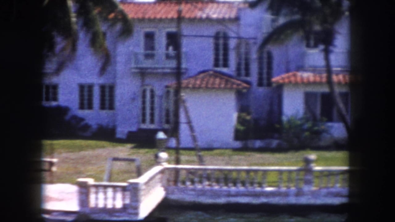 Mediterranean Revival mansion with terracotta tile roof and white stucco facade behind a white balustrade waterway wall; Tampa, Florida, c.1960 8mm home movie.