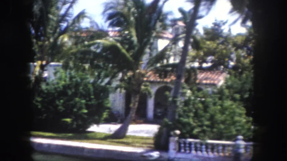 Mediterranean Revival home partially screened by palm trees with white balustrade in foreground; Tampa, Florida, c.1960 8mm film.