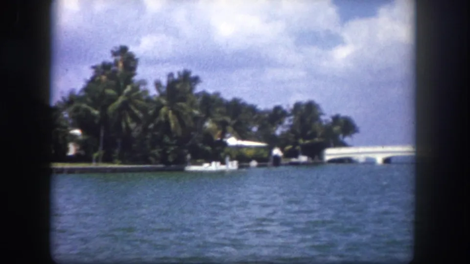 Open bay or inlet with tropical vegetation on a point of land, white balustrade at left edge, distant bridge-like structure; Tampa area waterway, c.1960 8mm film.