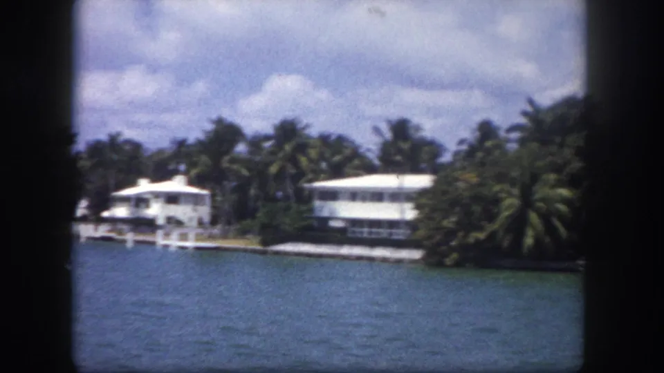 8mm home movie circa 1960 Tampa: a pan reveals multiple low white structures set behind tropical palms along a calm waterfront.