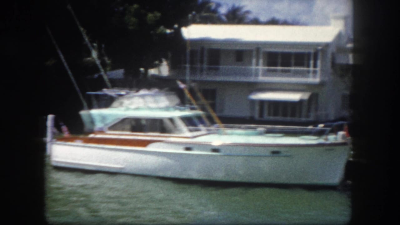 Classic cabin cruiser moored on a canal beside a two-story white waterfront house with a balcony