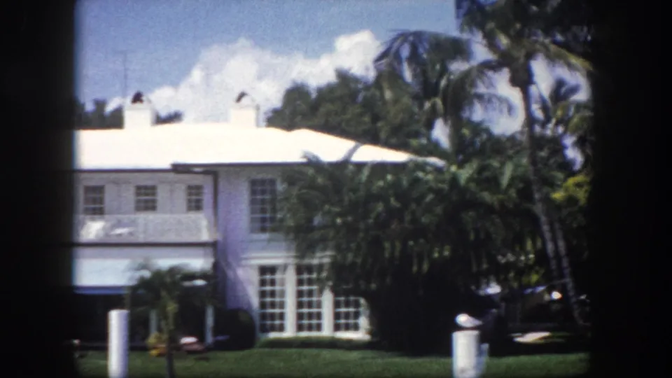 8mm film frame of a large white two-story Florida residence with palm trees and lawn, shot from a moving car, circa 1960 Tampa.