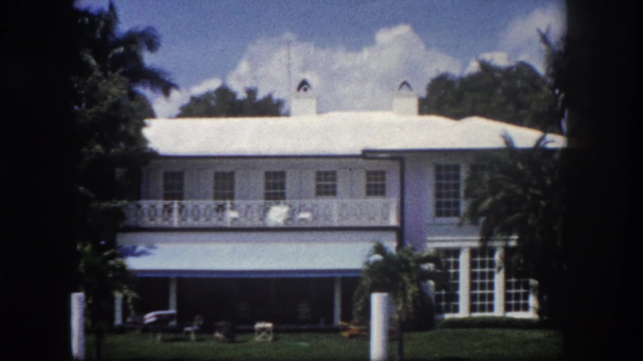 8mm film frame of a large white Florida residence showing decorative upper-floor balcony railing and covered ground-floor porch, circa 1960 Tampa.
