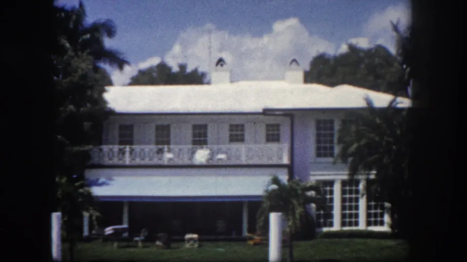 8mm film frame of a large white Florida residence showing decorative upper-floor balcony railing and covered ground-floor porch, circa 1960 Tampa.