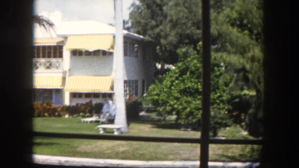 8mm home movie, c.1960 Tampa, Florida — mid-century two-story white building with yellow-striped awnings surrounded by tropical garden and lawn.