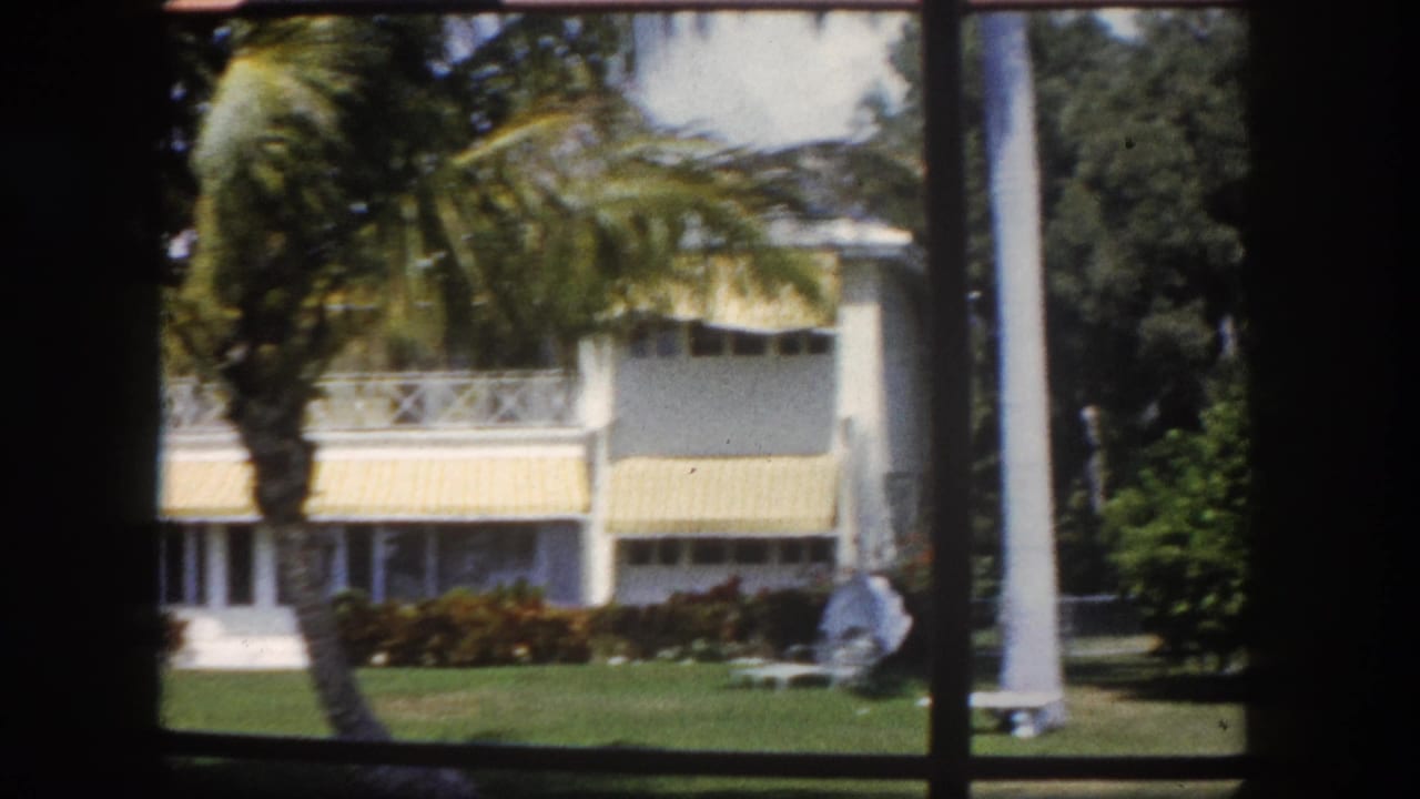 White stucco house with yellow-striped awnings and palm trees, viewed through a window frame.