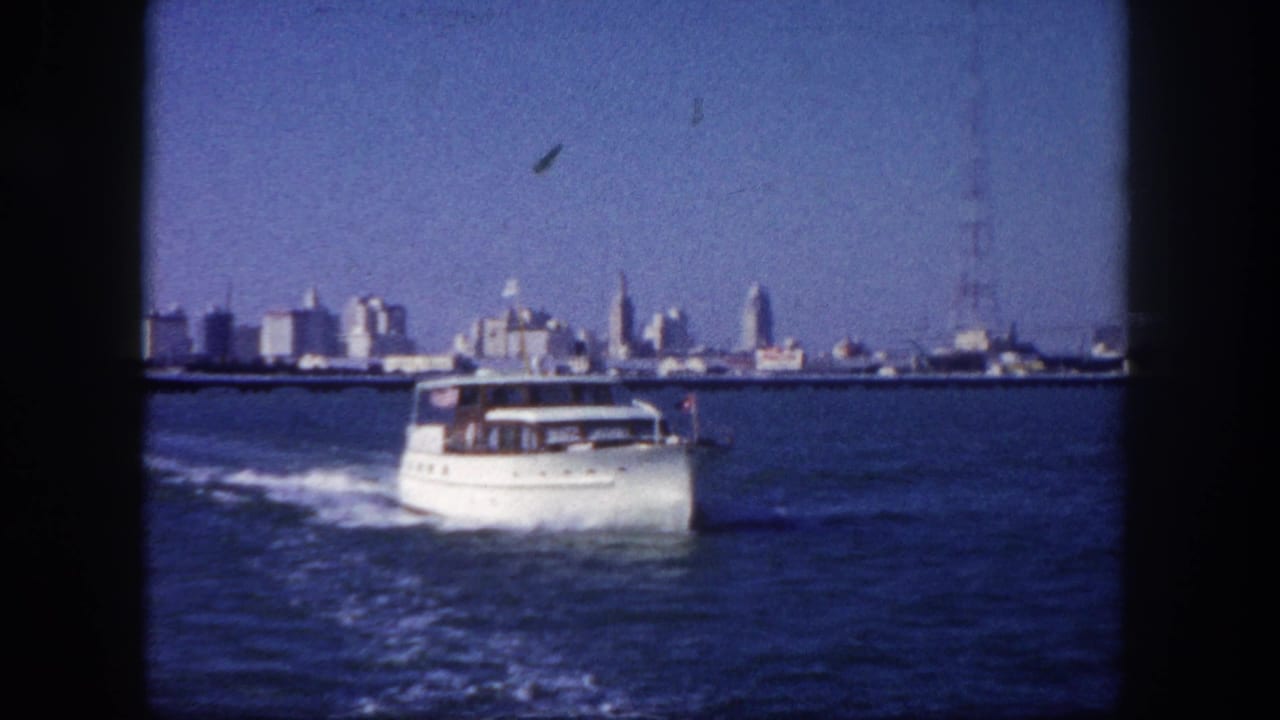 White cabin cruiser under way on Tampa Bay, circa 1960, with mid-century downtown skyline and a tall antenna tower visible across the water.