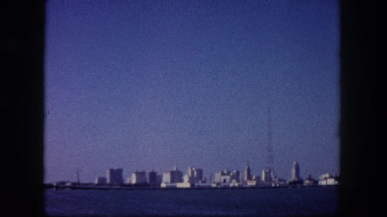 Tampa, Florida downtown skyline seen from open water circa 1960, mid-century buildings spread across the far shore under a broad blue sky.