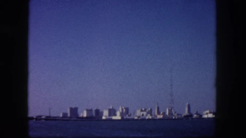 Tampa, Florida downtown skyline seen from open water circa 1960, mid-century buildings spread across the far shore under a broad blue sky.