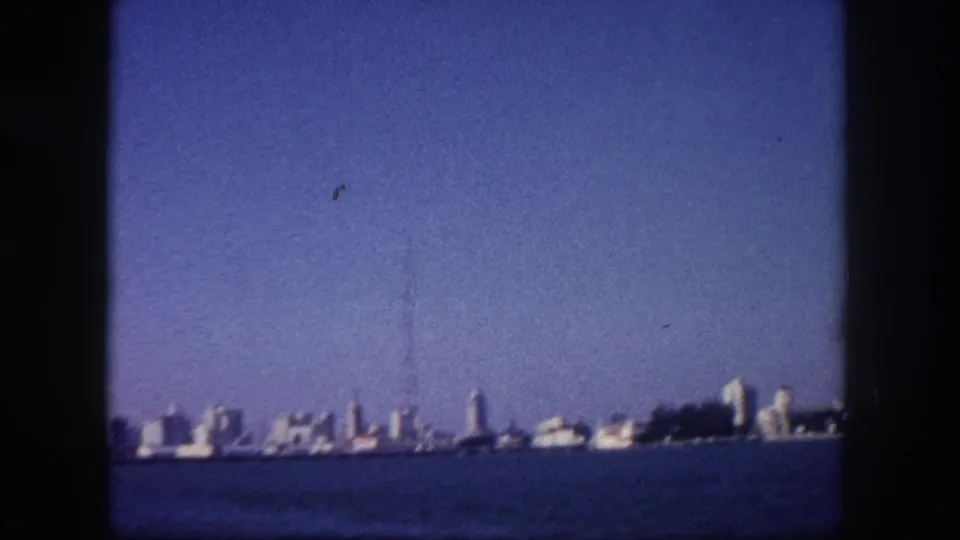 Tampa, Florida waterfront skyline circa 1960, with a prominent communications or broadcast tower rising above the mid-century building line, shot from the water.