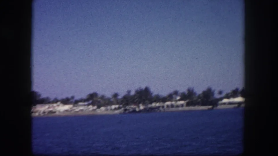 8mm footage of a palm-lined Florida coastal community viewed from a boat, with low buildings and open water visible, circa 1960.
