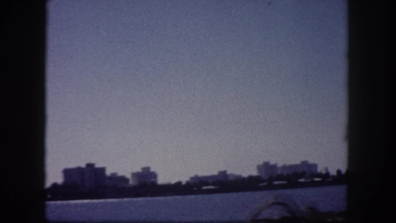 1960 Tampa Bay pan shot showing waterfront skyline with mid-rise buildings and a curved bridge arch in blue-tinted 8mm film.