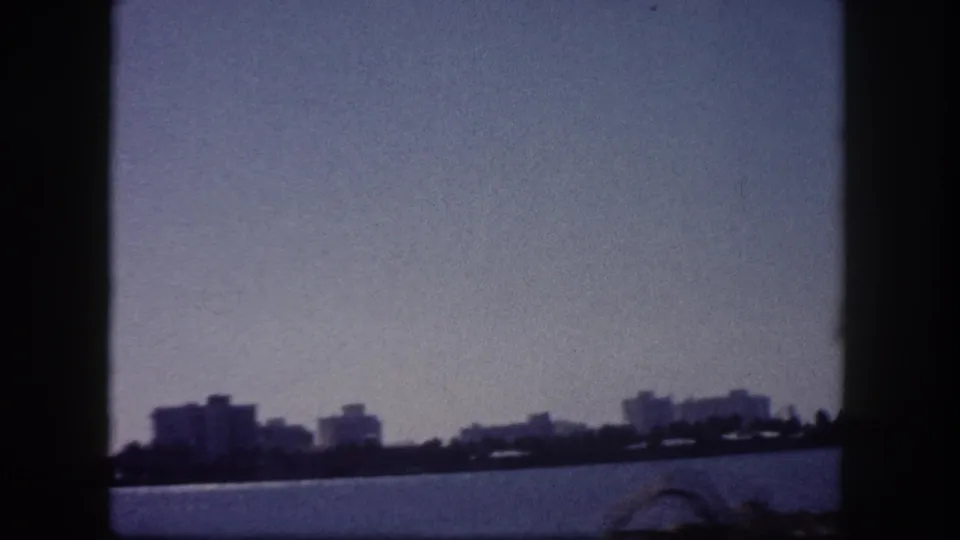 1960 Tampa Bay pan shot showing waterfront skyline with mid-rise buildings and a curved bridge arch in blue-tinted 8mm film.
