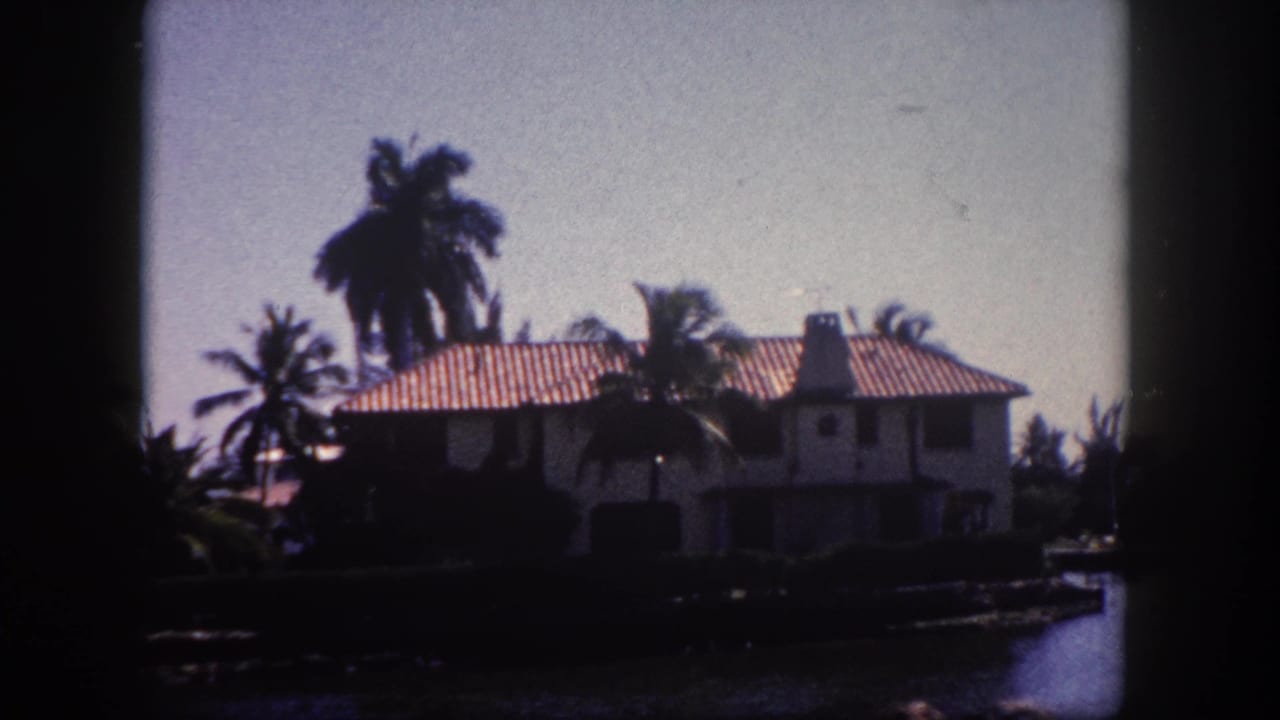 Two-story Mediterranean Revival stucco house with terracotta tile roof and canal frontage, filmed on 8mm in Tampa, Florida, circa 1960.