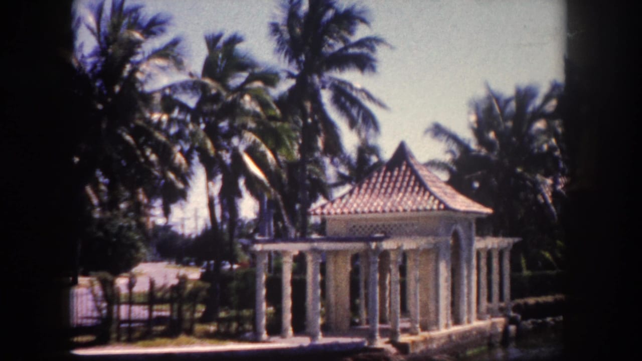 Decorative stone-columned gazebo with tiled hip roof photographed amid palm trees on 8mm film, Tampa, Florida, circa 1960.