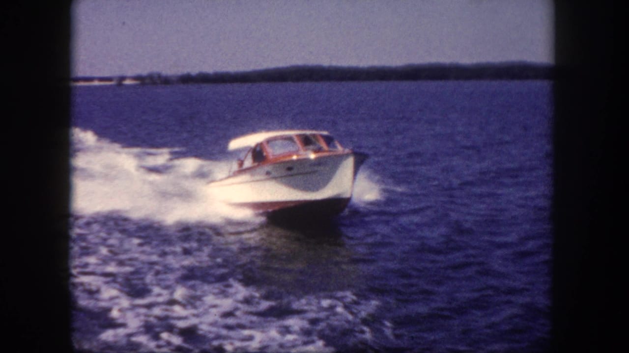8mm home movie of a white cabin cruiser with mahogany trim at speed on open water, distant tree-lined shoreline on the horizon, circa 1960.