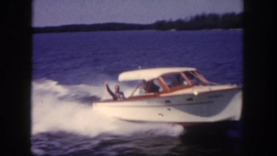 8mm home movie close-up of a white motorboat with wood cabin trim at speed, helmsman figure visible at the wheel, Florida waterway circa 1960.