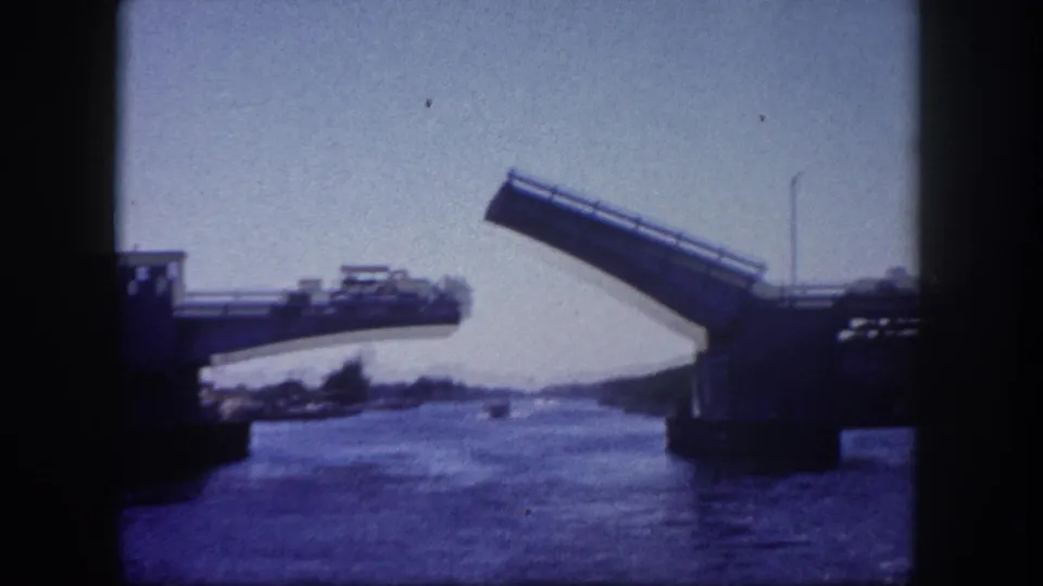 8mm frame, c. 1960, Tampa, Florida: raised bascule drawbridge leaf angled upward over the waterway channel, bridge roadway and abutments visible.