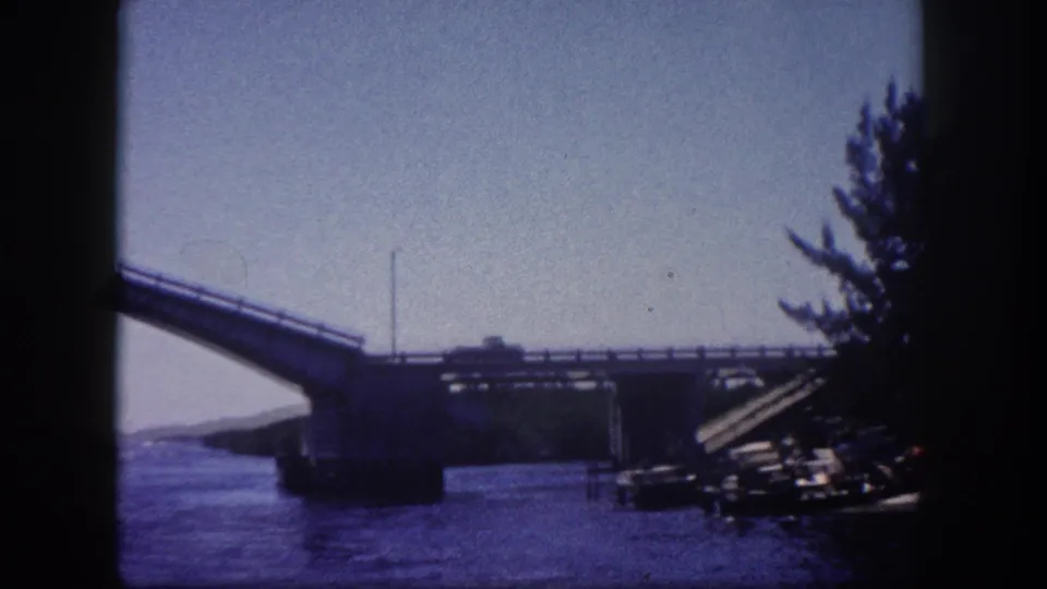 Bascule drawbridge spans raised over a waterway in Tampa, Florida, circa 1960; structural or dock elements visible at right edge, tree line at upper right, 8mm film.