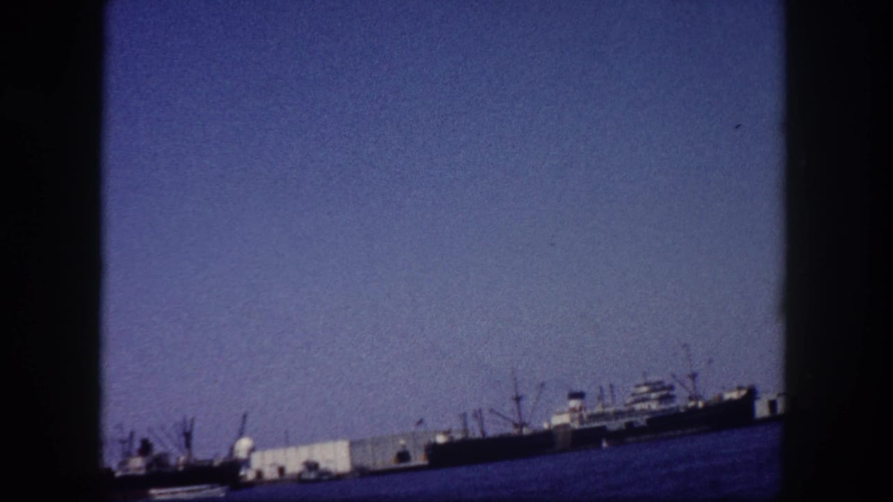 Cargo ships and dock cranes at Tampa, Florida seaport captured on 8mm home-movie film circa 1960, with visible grain and cool color shift.