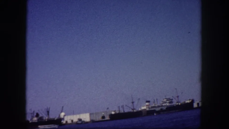 Cargo ships and dock cranes at Tampa, Florida seaport captured on 8mm home-movie film circa 1960, with visible grain and cool color shift.