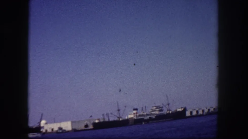 Tampa, Florida seaport viewed from the water circa 1960, ships and dock structures along the horizon with clear sky dominating the frame on 8mm film.