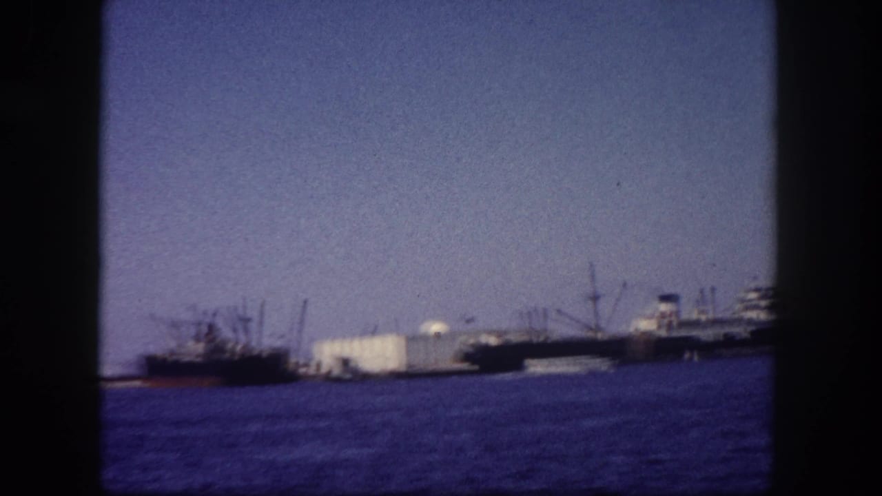 Multiple cargo vessels moored at Tampa port, Florida, circa 1960, photographed on 8mm film with blue-violet color cast and film frame border visible.