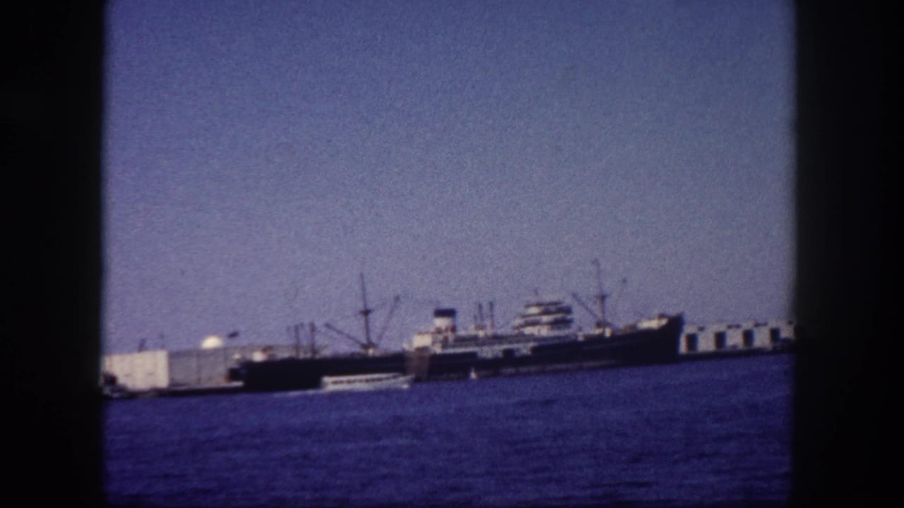 Cargo ships and loading cranes at Tampa port, Florida, circa 1960, on 8mm film; blue-purple dye cast and visible grain throughout.