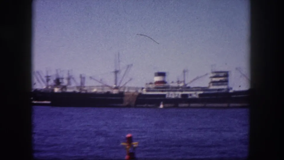 Fabre Line liner and adjacent cargo vessels at Tampa port, Florida, circa 1960; red-orange buoy in foreground, cranes visible, 8mm film grain throughout.
