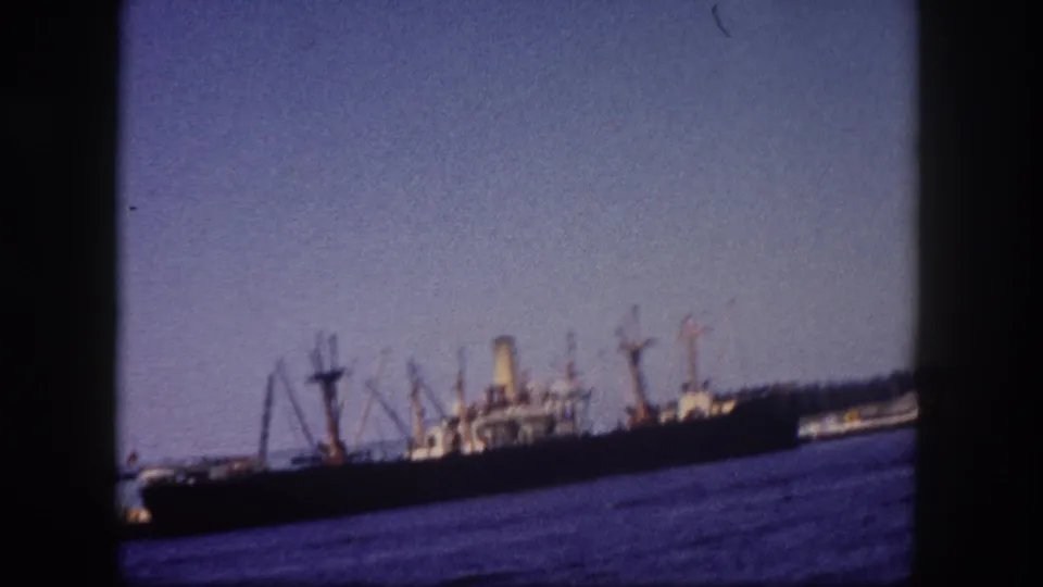 Cargo vessel at Tampa port dock, circa 1960, with multiple loading derricks, characteristic 8mm blue-purple water rendering.