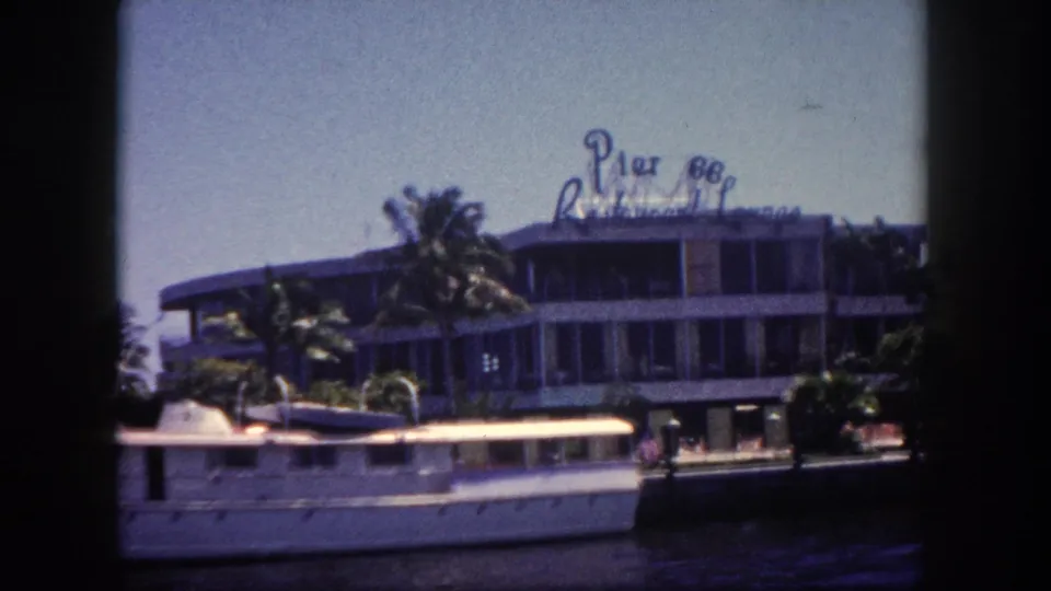 8mm film frame, circa 1960, of what appears to be the Pier 88 Restaurant Lounge on the Tampa, Florida waterfront, viewed from water with a large white vessel docked alongside.