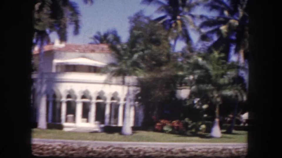 White Mediterranean Revival mansion with arched colonnade, terracotta tile roof, and red flowering shrubs, Tampa, Florida, circa 1960, 8mm film.