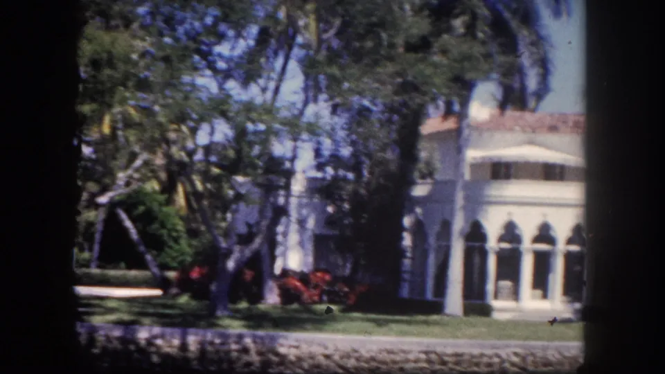 Mediterranean Revival home with open arched arcade and red flowering plants in the foreground, Tampa, Florida, circa 1960, 8mm film.