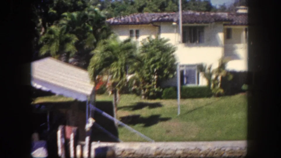 Left side of a two-story Mediterranean-style house with palm trees and tropical lawn, 8mm home movie, Tampa Florida area, c.1960.