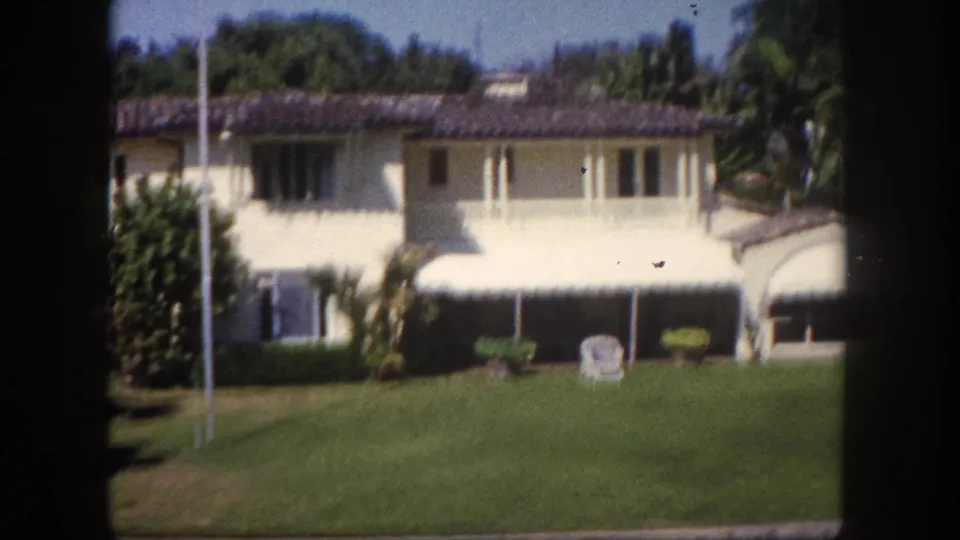 Two-story Mediterranean-style house with striped awning and lounge chair on lawn, 8mm home movie, Tampa Florida area, c.1960.
