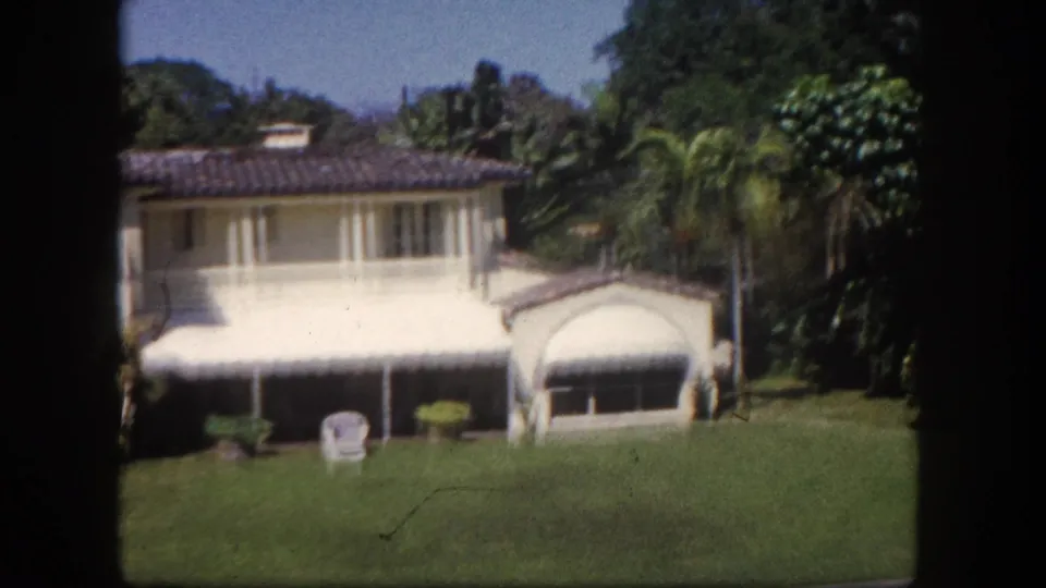 Right section of two-story Mediterranean-style house with striped awnings and tropical garden, 8mm home movie, Tampa Florida area, c.1960.