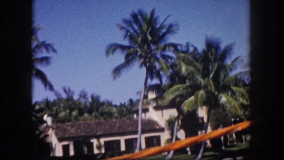 8mm home movie frame circa 1960 showing a canal-side stucco house under palm trees in Tampa, Florida, filmed from a watercraft.