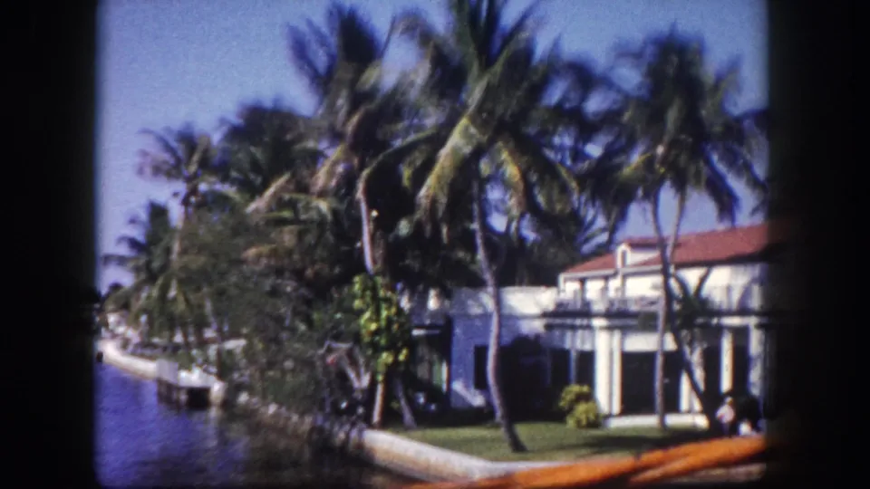 8mm color film frame circa 1960 revealing a residential canal lined with palms and a two-story stucco house with terracotta roof, Tampa, Florida.