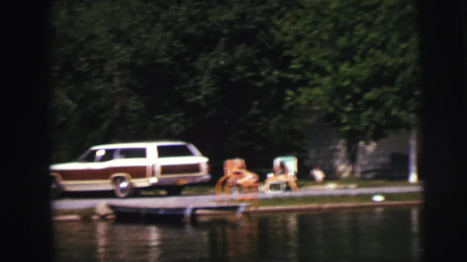1976 8mm footage from Lynbrook, New York — wood-paneled station wagon, people relaxing in lawn chairs, and a small boat at a waterfront dock.