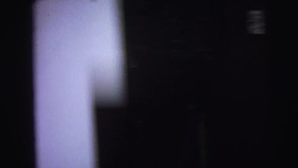 Near-black 8mm home-movie frame, likely a pan between rooms during filming; Lynbrook, New York, circa 1976.